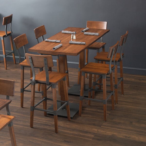 A Lancaster Table & Seating wooden bar table with chairs and napkins.