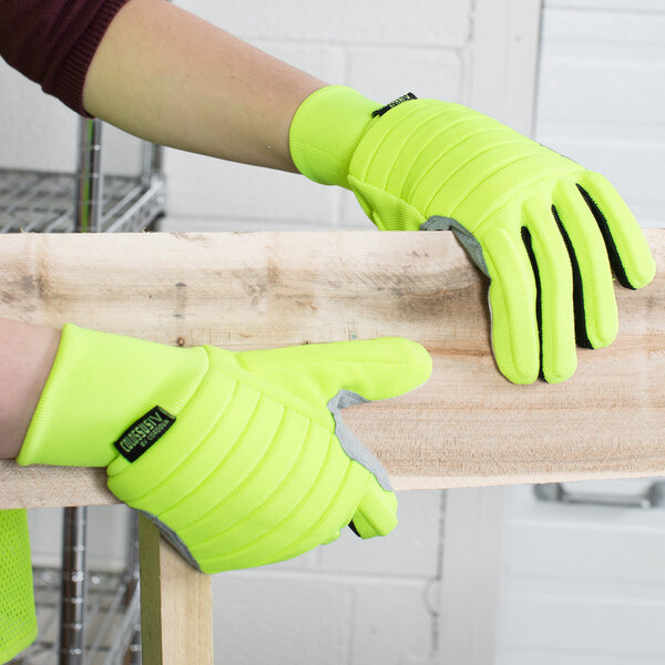 A person wearing Cordova Colossus IV Hi-Vis lime gloves with canvas palm coating holding a piece of wood.
