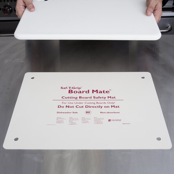 A person holding a San Jamar white cutting board mat on a counter.