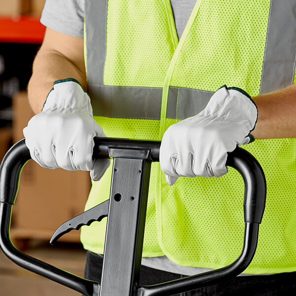 A person wearing Cordova gray leather driver's gloves and a safety vest holding a forklift.