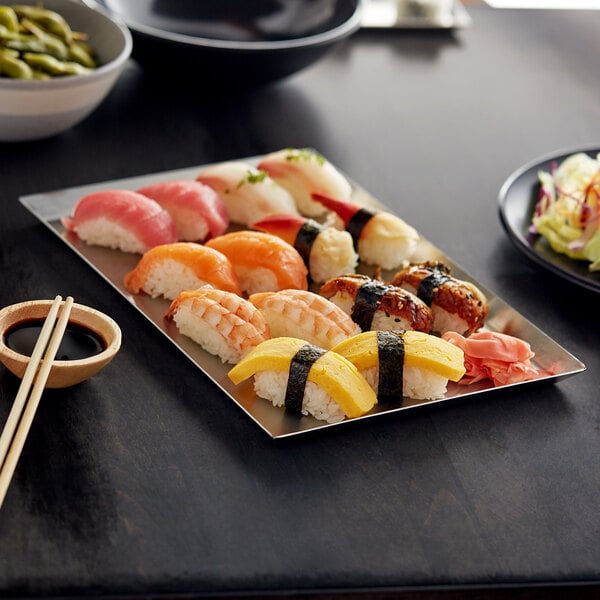 An Acopa rectangular stainless steel tray with sushi rolls and chopsticks on a table.