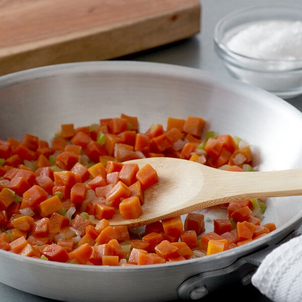 A wooden spoon in a pan with diced carrots and celery.