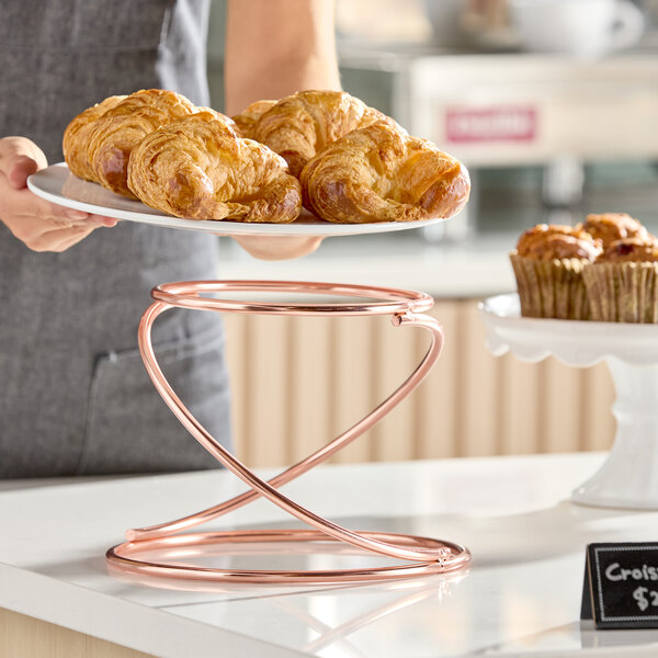 A rose gold swirl metal display stand designed to hold plates or trays for serving food.