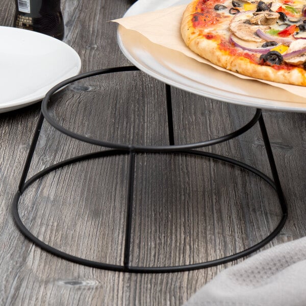 A pizza on a plate with a black metal display stand under it.