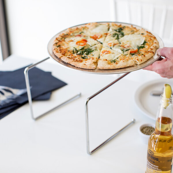 A hand using a Chrome Metal Pizza Stand to hold a plate of pizza.