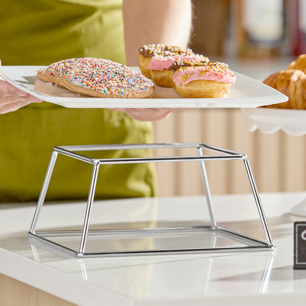 A square stainless steel metal display stand with a minimalist open-frame design.