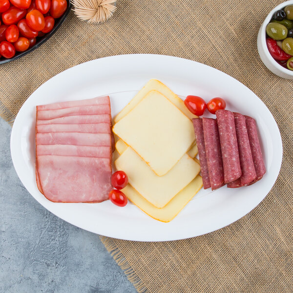 A white plastic oval catering tray with sliced meat, cheese, and tomatoes.