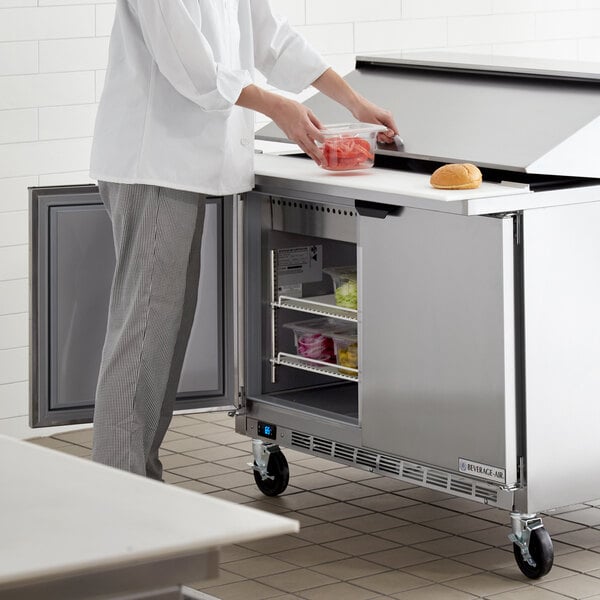 A chef using a Beverage-Air sandwich prep table to store food on a white counter.