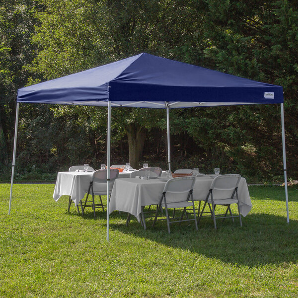 A navy Caravan Canopy tent with a table and chairs set up on grass.