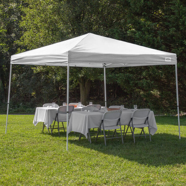 A white Caravan Canopy with tables and chairs set up in the grass.