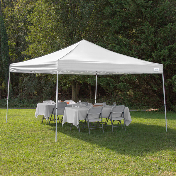 A white Caravan Canopy tent set up with white tables and chairs on grass.