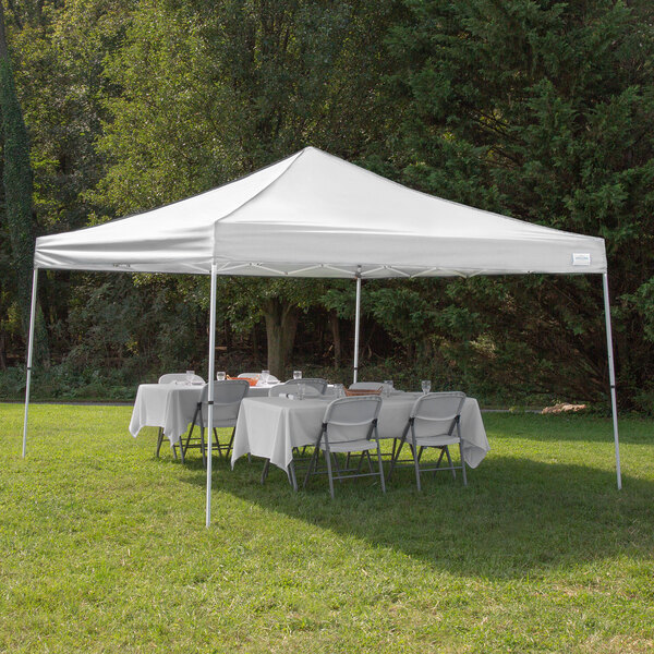 A white Caravan Canopy tent with tables and chairs set up in the grass.