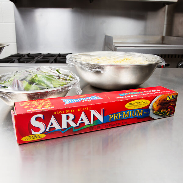 A red box of SC Johnson Saran Premium plastic wrap on a counter next to a bowl of salad.