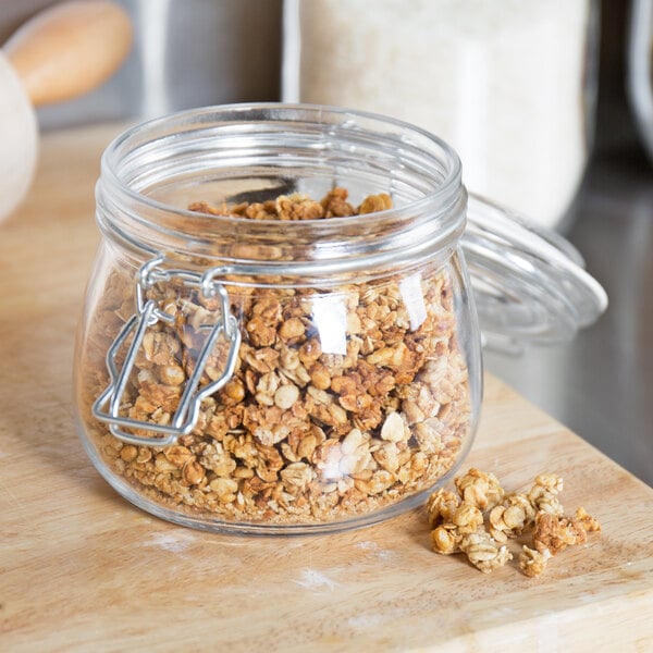 A Choice glass storage jar filled with granola on a cutting board.