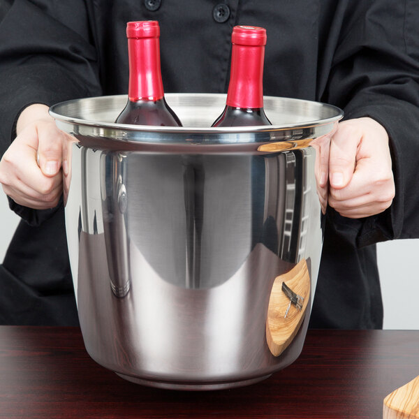 A person holding a Vollrath stainless steel double bottle wine bucket filled with red wine bottles.