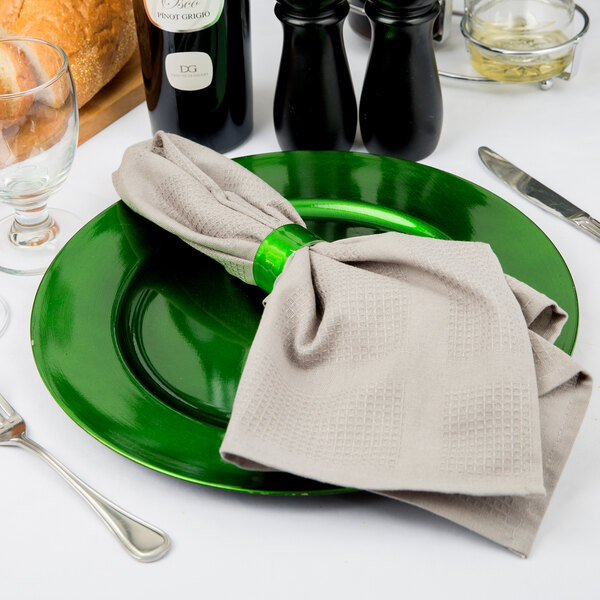 A green Tabletop Classics by Walco plastic charger plate with a napkin and silverware on it.