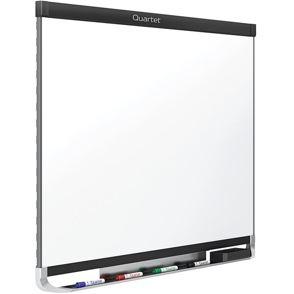 A Quartet magnetic porcelain white board with a black aluminum frame and markers on it.
