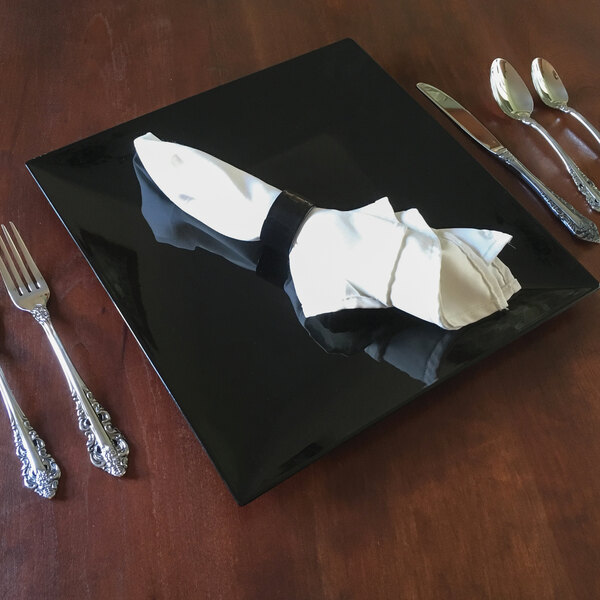 A black square Tabletop Classics by Walco charger plate with a napkin, spoon, and fork on it.