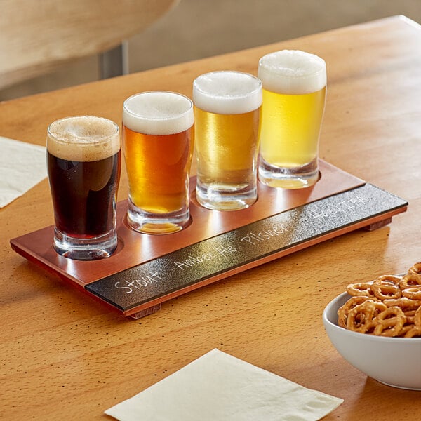 An Acopa Write-On flight tray holding beer glasses with a bowl of pretzels on a table.