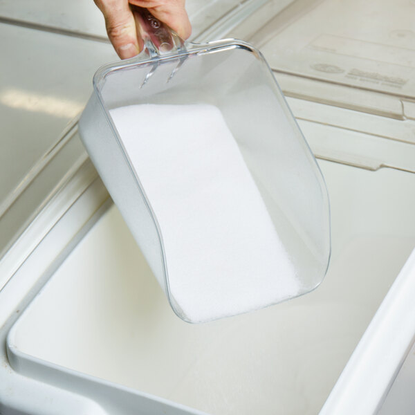 A hand using a Rubbermaid clear plastic utility scoop to pour white powder into a container.