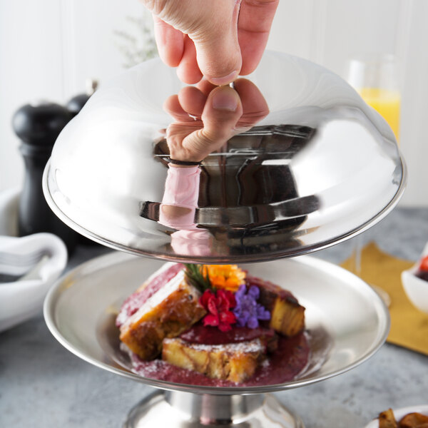 A hand using a Town stainless steel compote dish cover to serve food on a silver platter.