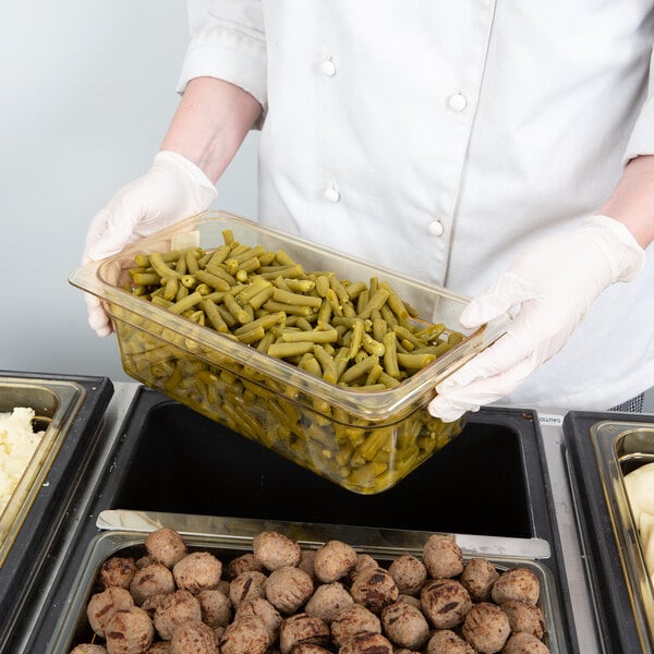 A person in white gloves holding a Cambro H-Pan of green beans.