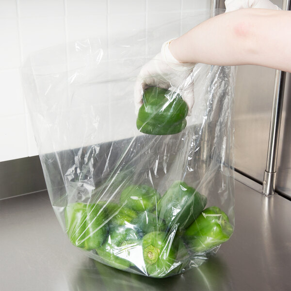 A hand holding a plastic bag of green peppers.