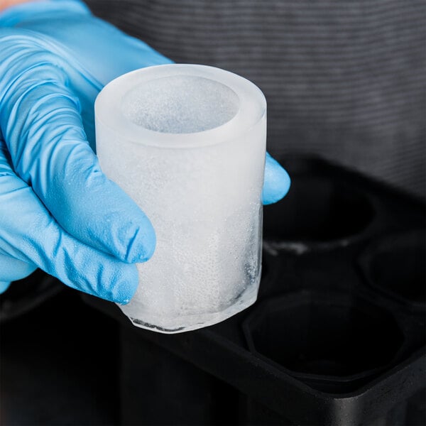 A person in blue gloves using a Tablecraft Black Silicone shot glass ice mold to make ice.