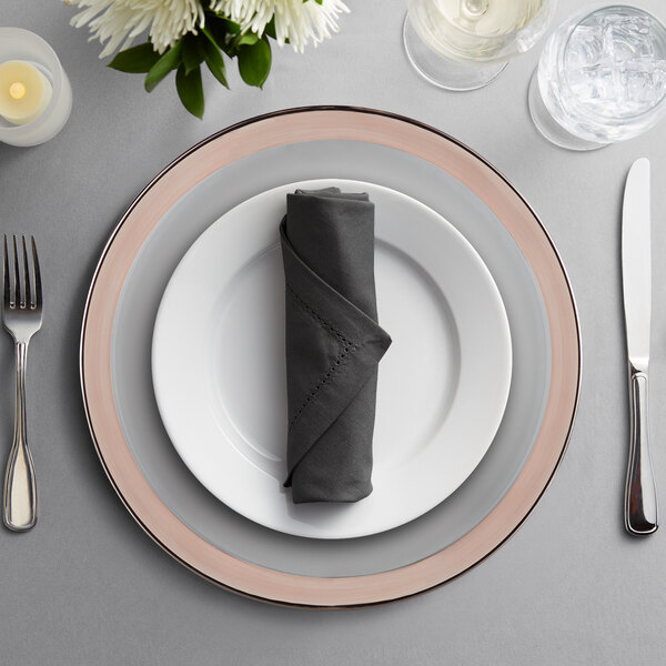 A table set with Charge It by Jay clear glass charger plates with copper rims, silverware, and a napkin.