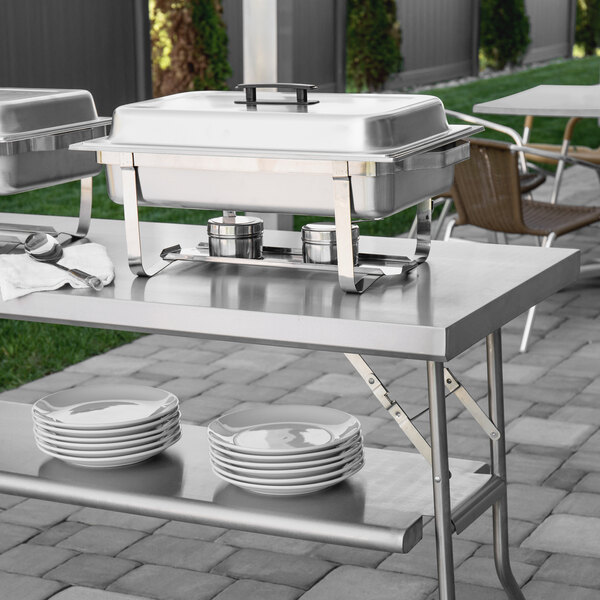 A Regency stainless steel folding work table with a buffet set up including plates and bowls.