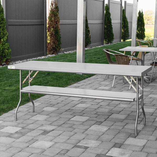 A Regency stainless steel folding table with a white tablecloth on a brick patio.