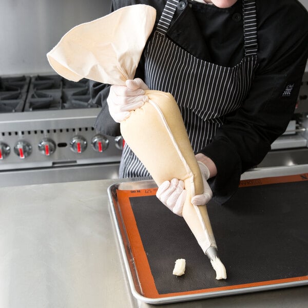 A person in a black and white apron using an Ateco canvas pastry bag to pipe pastries.