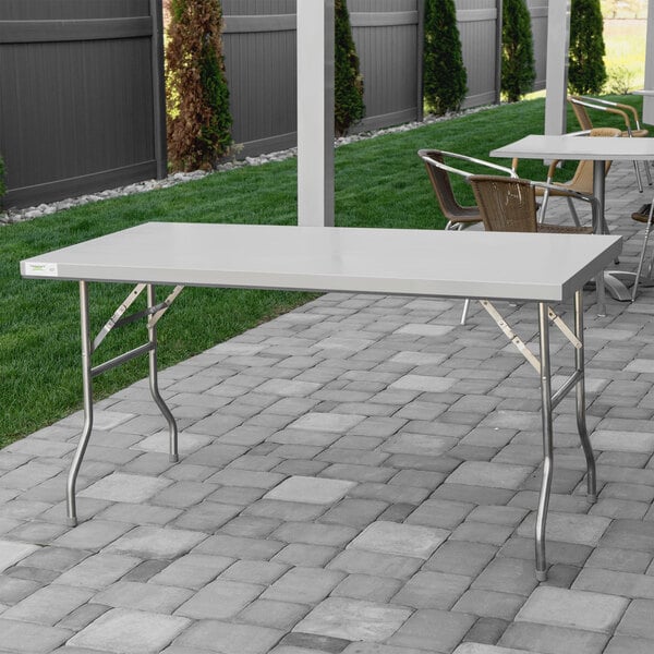 A Regency stainless steel folding work table on a brick patio.