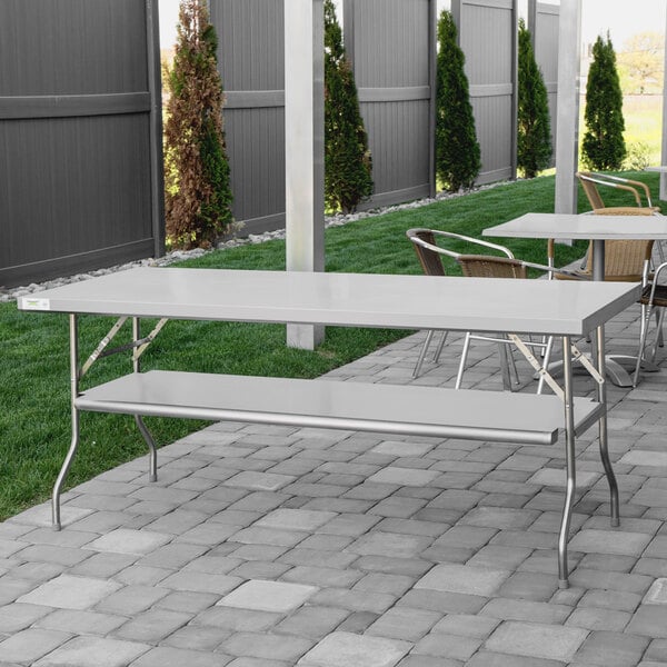 A Regency stainless steel folding work table with a removable undershelf set up on a patio.