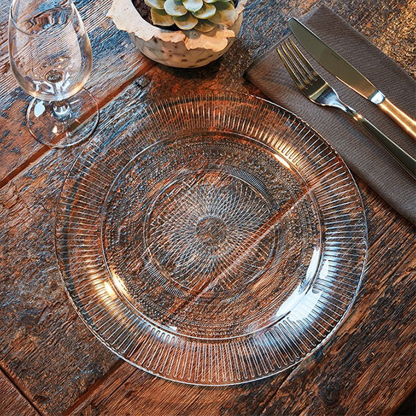 An Arcoroc Louison glass dinner plate with a fork and knife on a table.