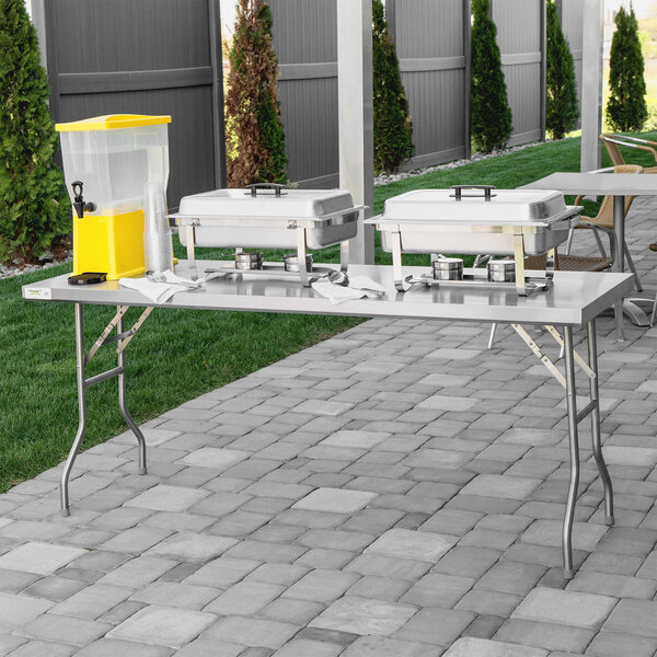 A Regency stainless steel folding work table on a stone walkway with food on it.