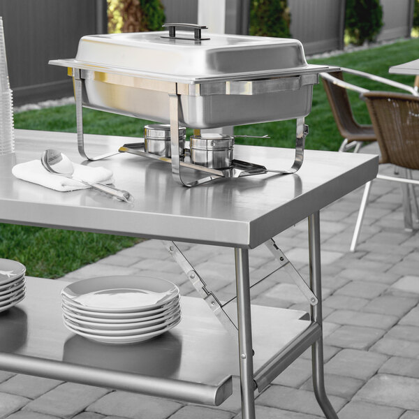 A Regency stainless steel folding work table with plates and silverware on it.