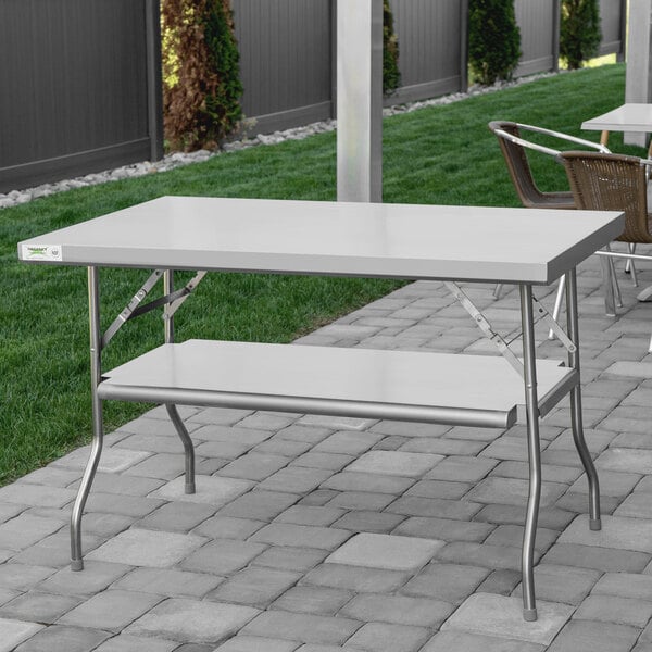 A Regency stainless steel folding table with a metal bar underneath on grass.