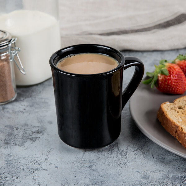 A black Libbey porcelain mug with a drink and a plate of bread and strawberries.