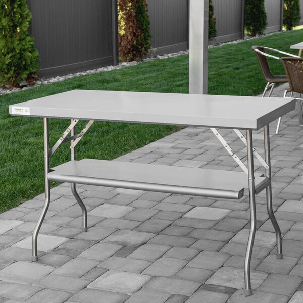 A Regency stainless steel folding work table with a metal bar on a brick patio.