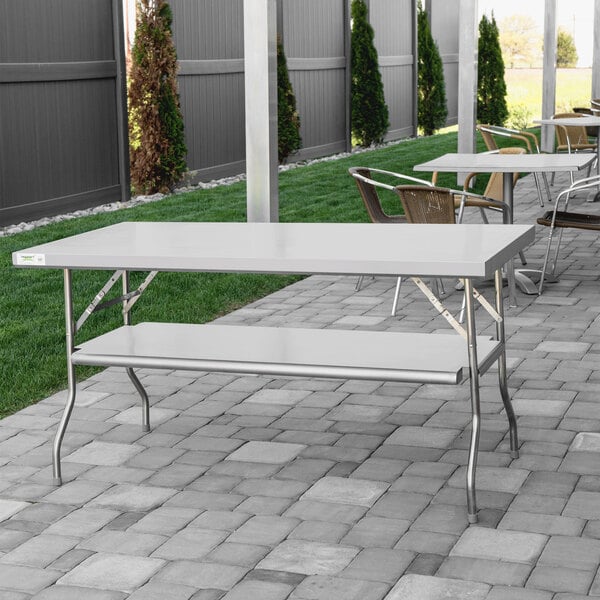 A Regency stainless steel folding work table with a removable undershelf on a stone patio.