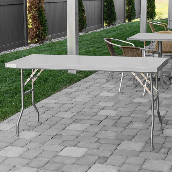 A Regency stainless steel folding work table on a stone patio.