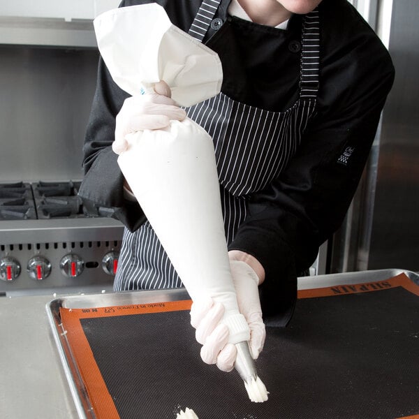 A woman in a black and white striped apron and gloves using an Ateco polyurethane coated pastry bag.