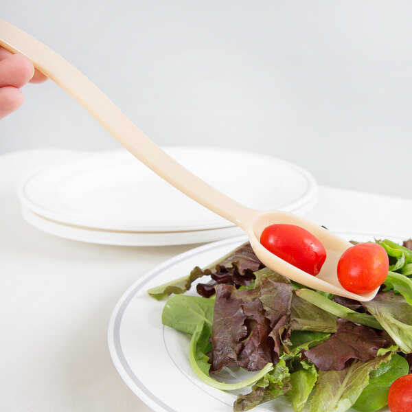 A person using a Cambro beige Camwear salad bar spoon to serve tomatoes on a plate of salad.