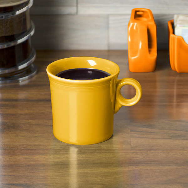 A yellow Fiesta china mug with a brown liquid on a wooden surface.