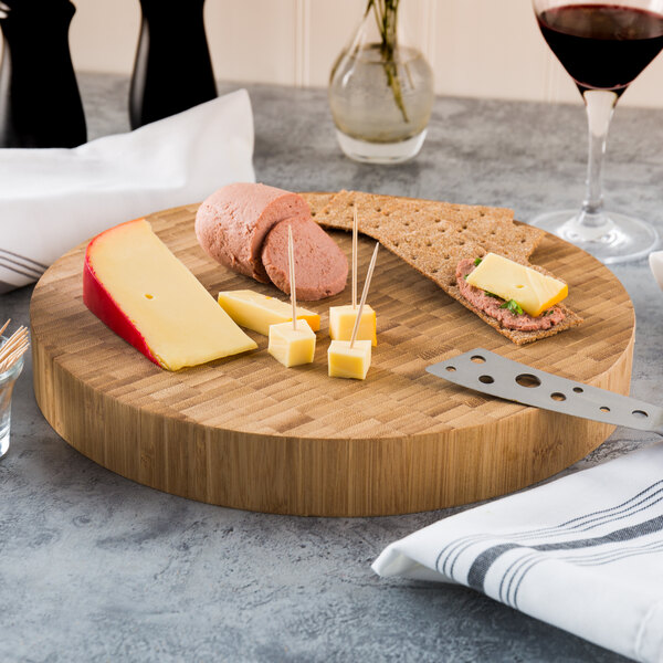 A bamboo cutting board with cheese and crackers on it.