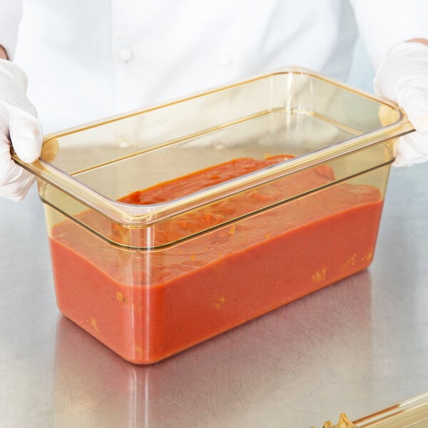 A person in gloves holding a Carlisle glass container filled with red sauce.