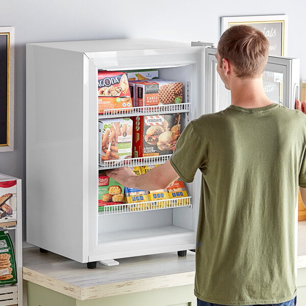 A man opening an Avantco white countertop display freezer with food inside.