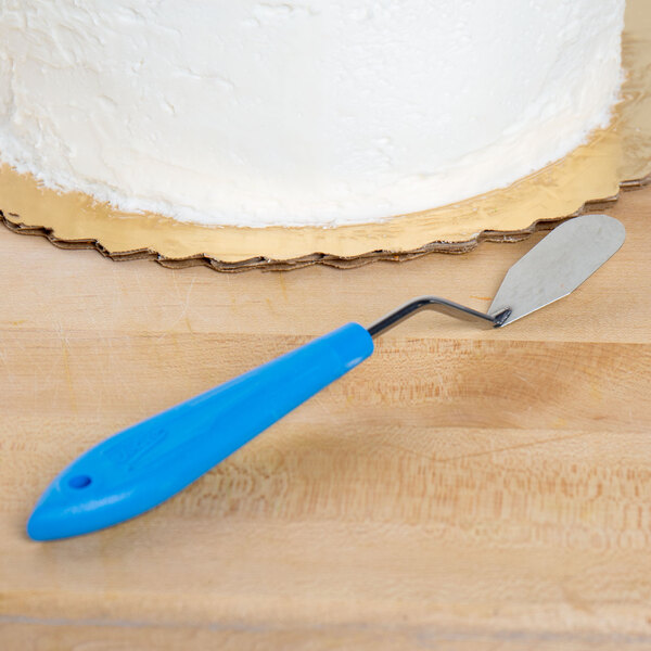 A cake with white icing and blue icing made with an Ateco baking spatula on a wood surface.