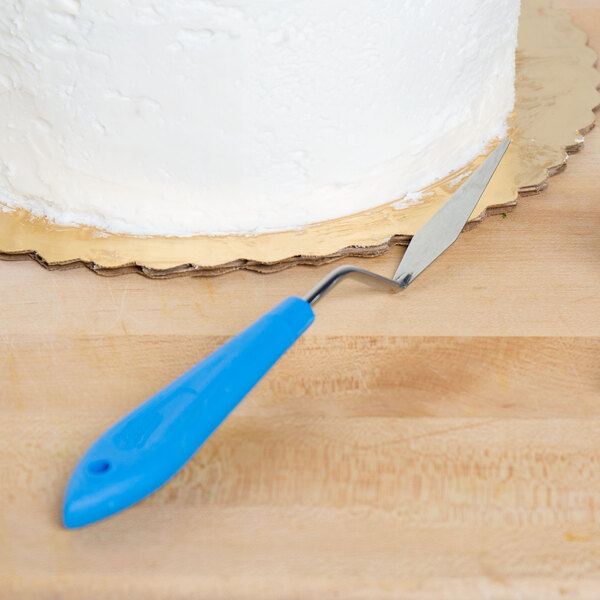 An iced cake with an Ateco offset spatula on a wooden table.